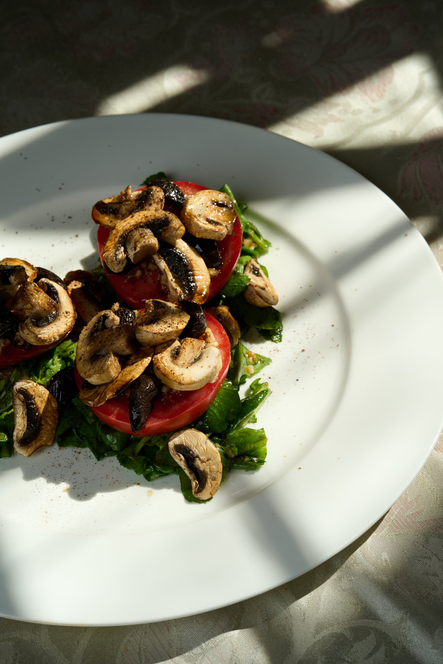 White plate with sunlit mushrooms, tomatoes, and greens